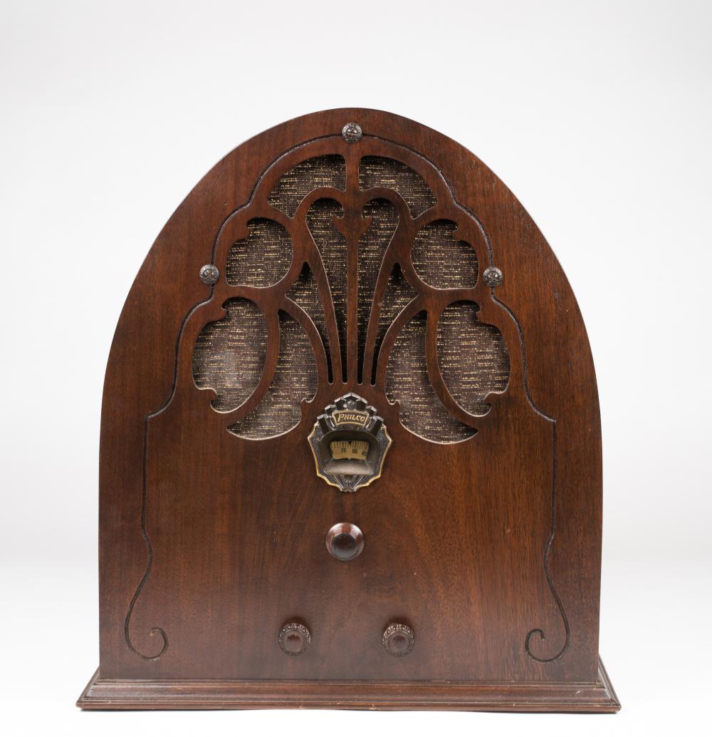 Front view of a vintage brown wooden cathedral-style radio with a decorative grille, “Philco” emblem, and four tuning knobs.