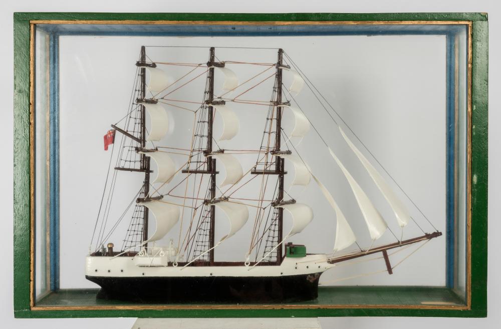 Scratch-built model sailboat with multiple masts and white sails displayed inside a framed glass case.