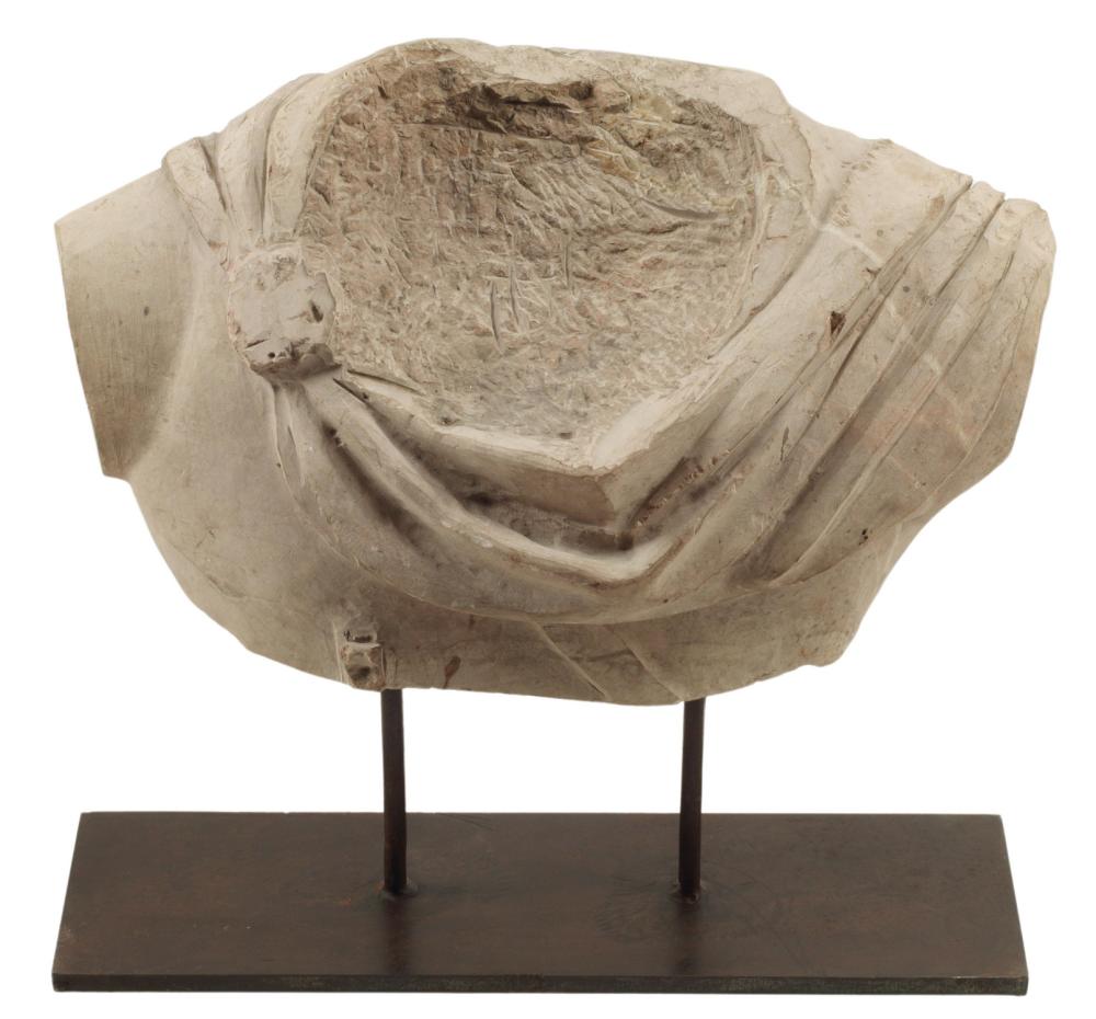 Marble sculpture fragment on a black stand, showing carved drapery and a curved relief panel.
