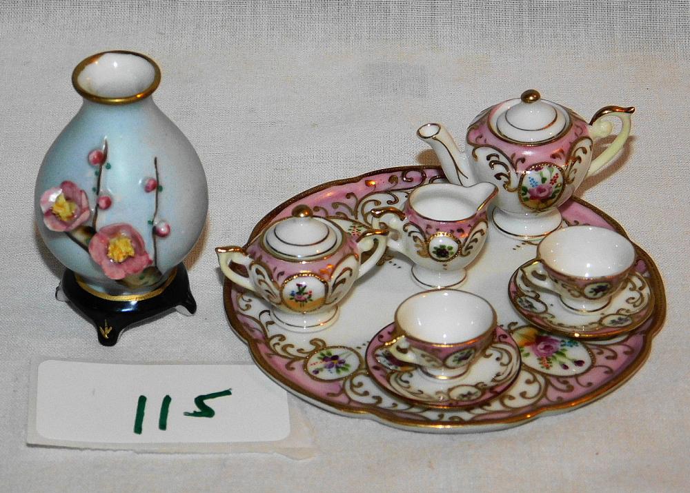 Vintage porcelain child’s tea set with teapot and cups on a decorative tray, plus a small vase with painted flowers.