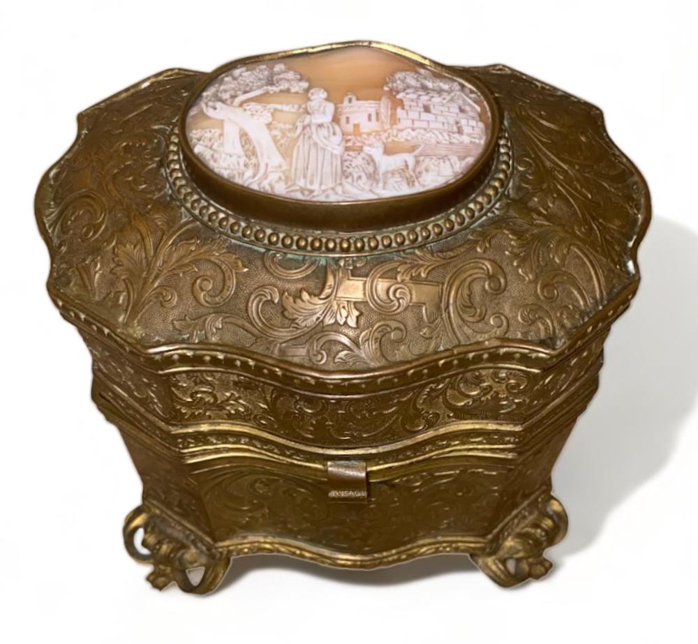 Bronze-colored decorative casket box with ornate scrollwork and a round cameo-style panel on top.