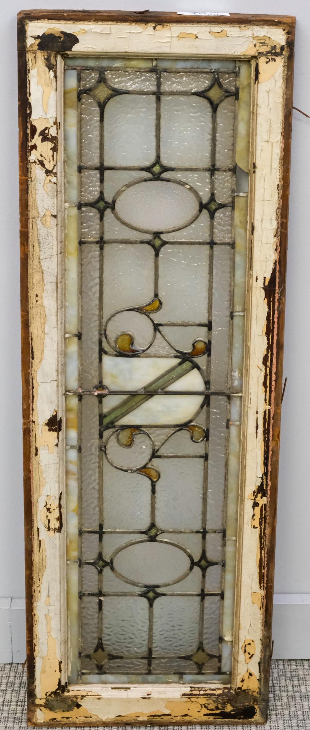 Antique stained glass window panel with leaded grid and clear, gray, and yellow-toned decorative shapes, shown upright in a wooden frame.