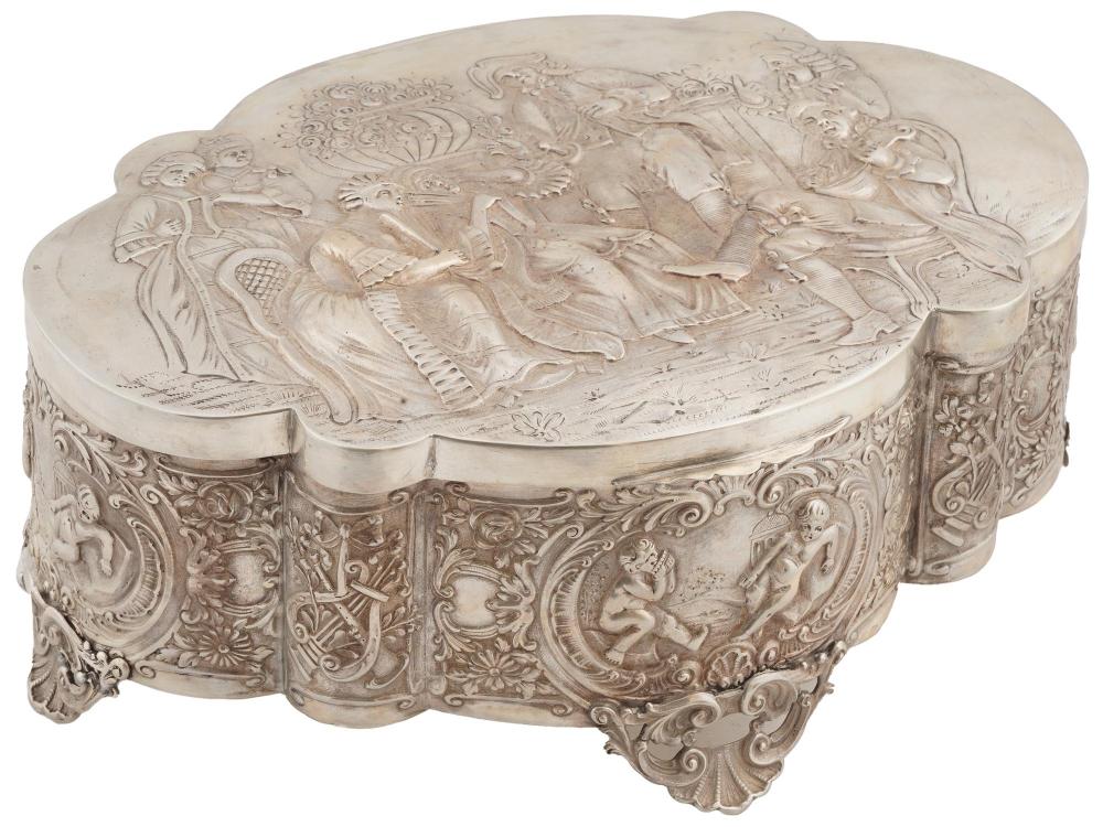 Ornate oval silver-toned jewelry box with embossed floral and figure relief on the lid and sides, hinged lid open edge visible.