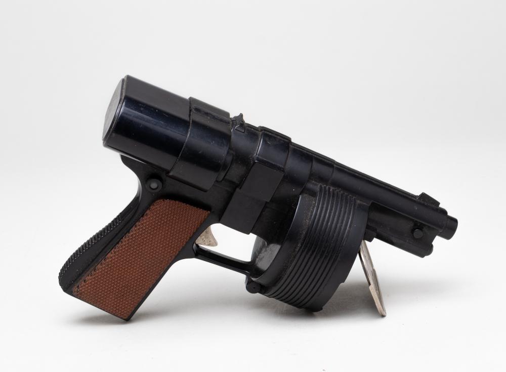 Black toy cap gun with a hinged brown grip and a cylindrical barrel, shown at an angle on a white background.