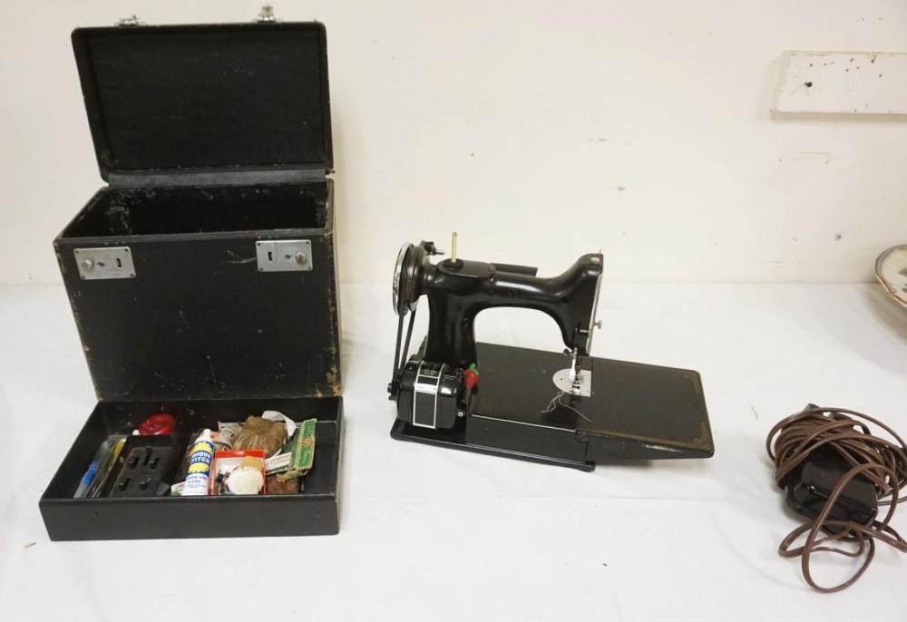 A black vintage sewing machine with a metal needle and presser foot, shown with an open case containing sewing accessories.