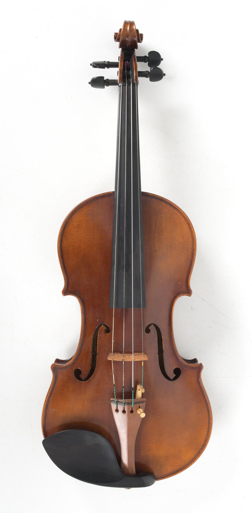 Front view of a wooden violin with brown varnish, f-holes, and four strings extending to the scroll.
