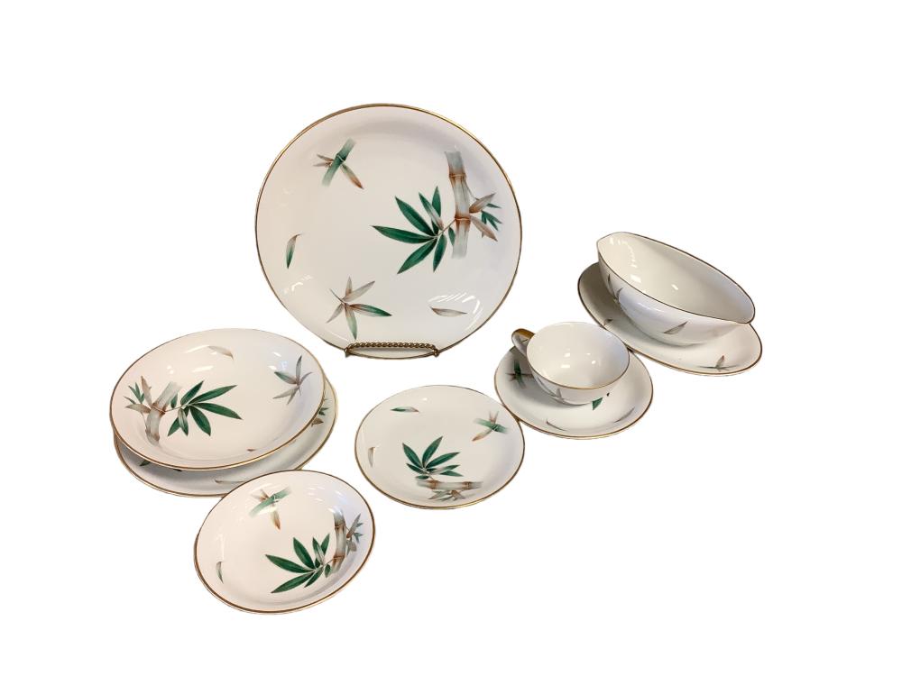 Set of white porcelain dinnerware pieces with a gold rim and green bamboo-and-stem floral decoration, photographed on a white background.