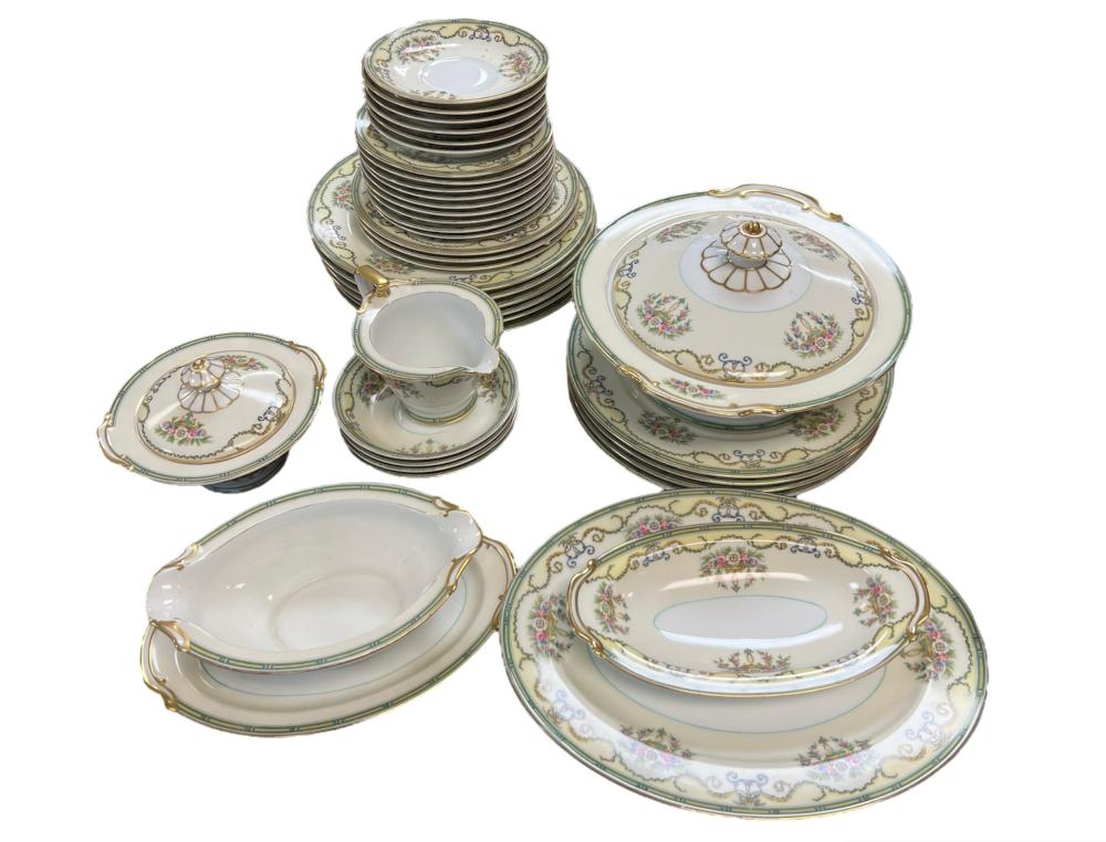 Stacked white porcelain dinner plates and serving dishes with gold trim and small floral bouquets, shown with a covered serving dish.