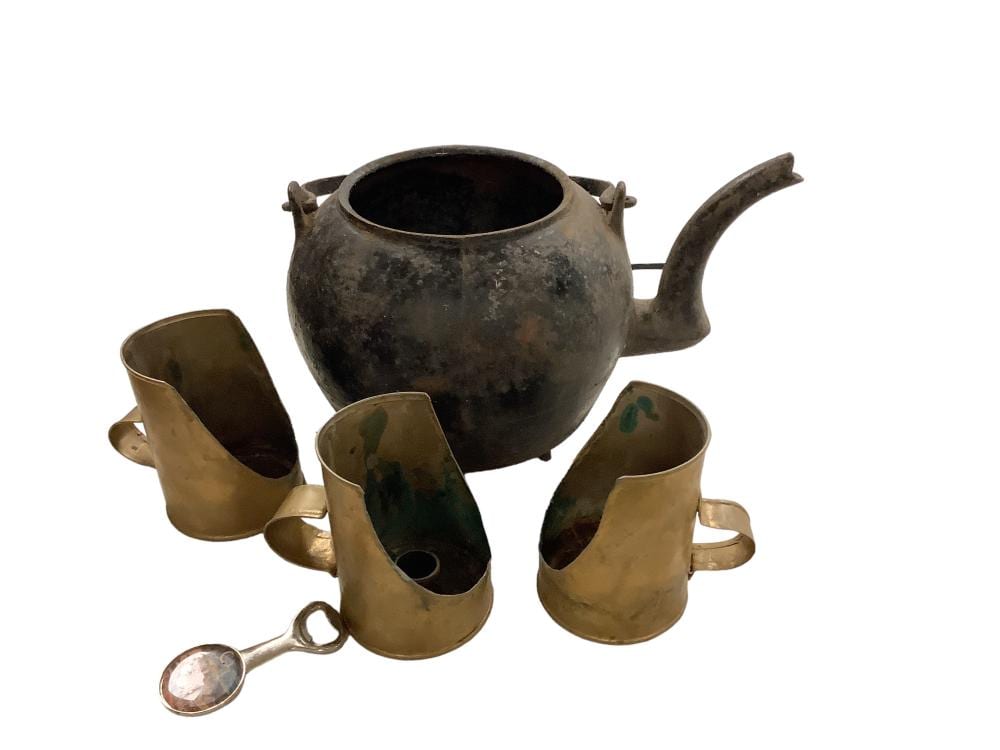 Rust-brown metal tea kettle with spout and handle, with four matching cup mugs and a small spoon resting beside it.