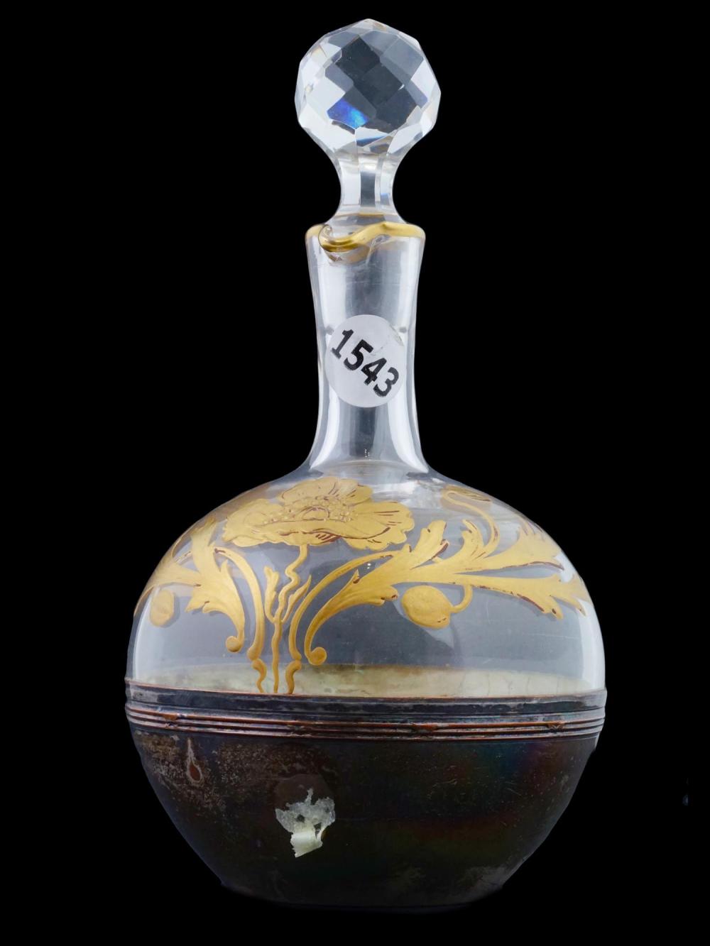Antique-style glass decanter with faceted stopper and gold floral design on the body, photographed against a black background.