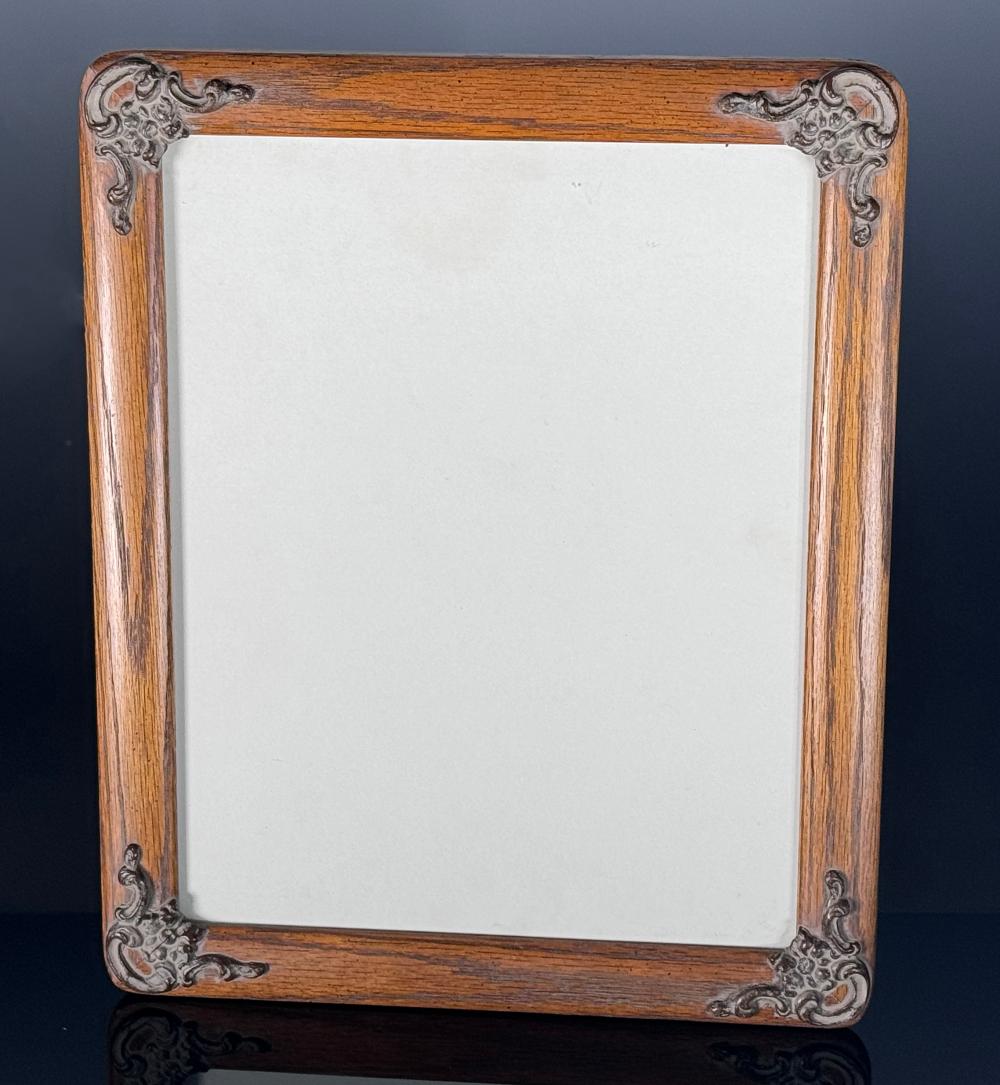 Wood picture frame with ornate metal corner scrollwork and an empty white backing, front view against a dark background.