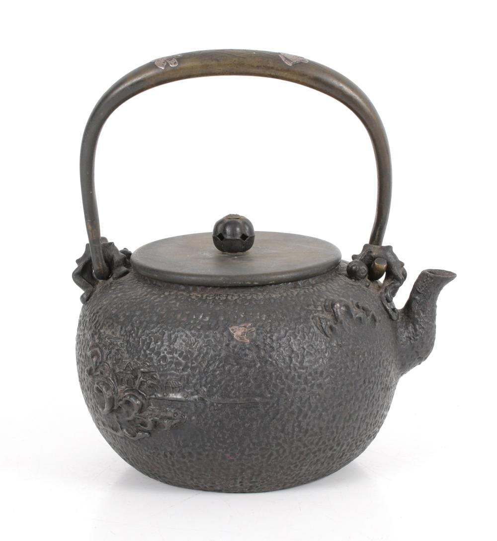 Japanese-style cast iron teapot with arched handle and round lid knob, dark gray hammered surface with raised decoration near the spout.