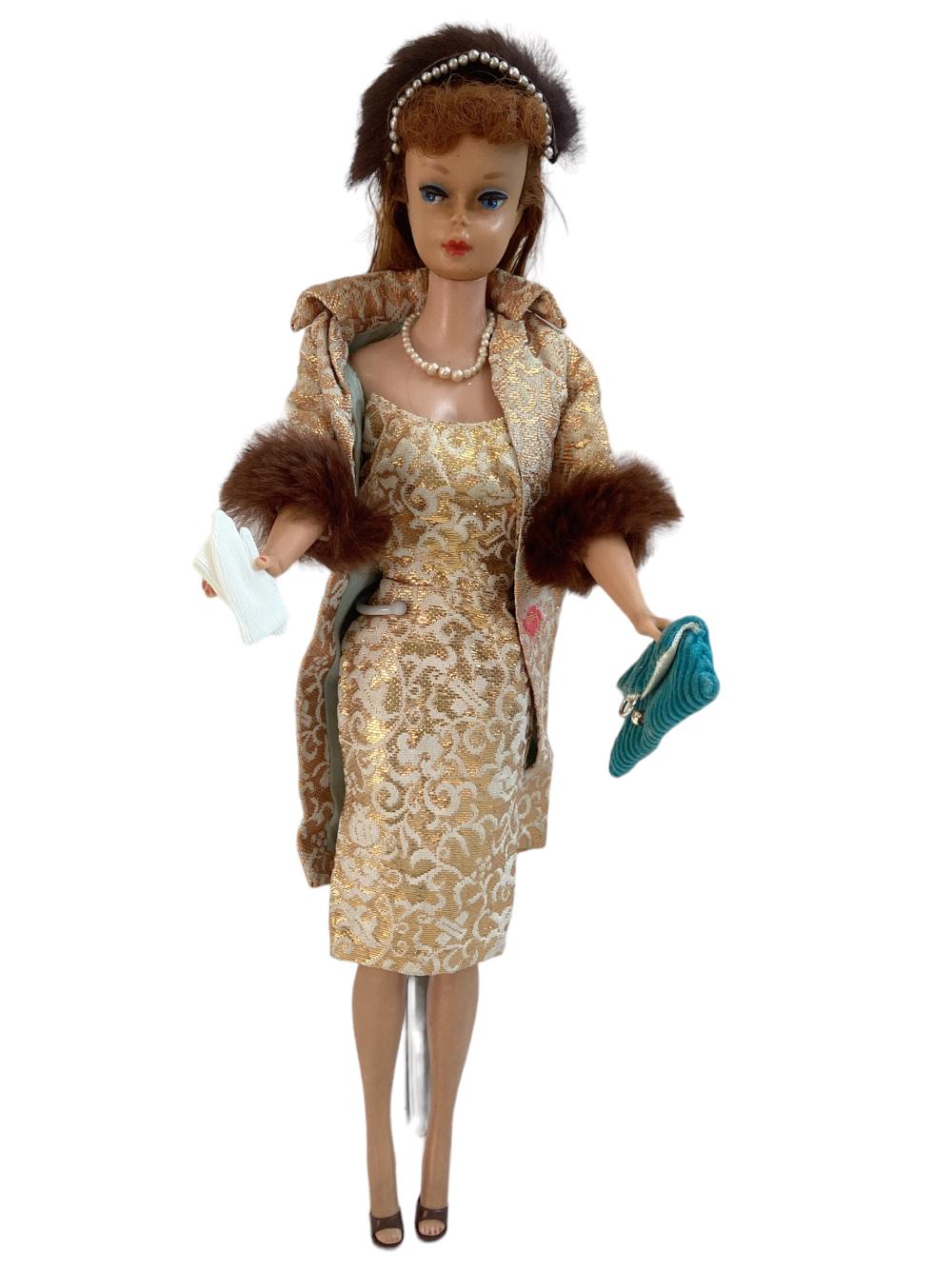 Fashion doll with brown updo, pearl headband, and gold patterned dress with fur-trimmed jacket, holding a booklet and a blue handbag.