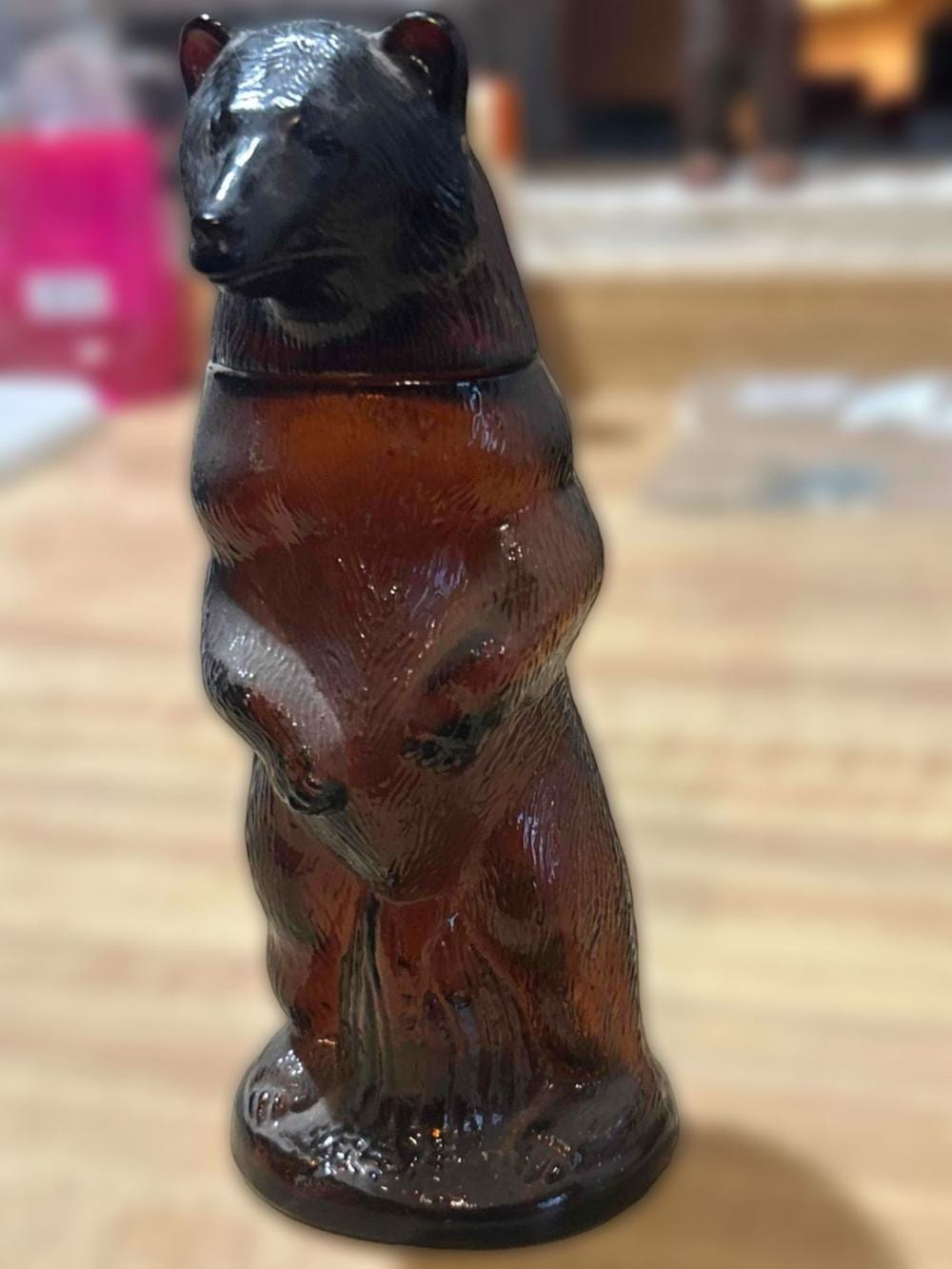 Brown bear-shaped bottle with a glossy finish and black cap, photographed close-up on a light wooden surface.