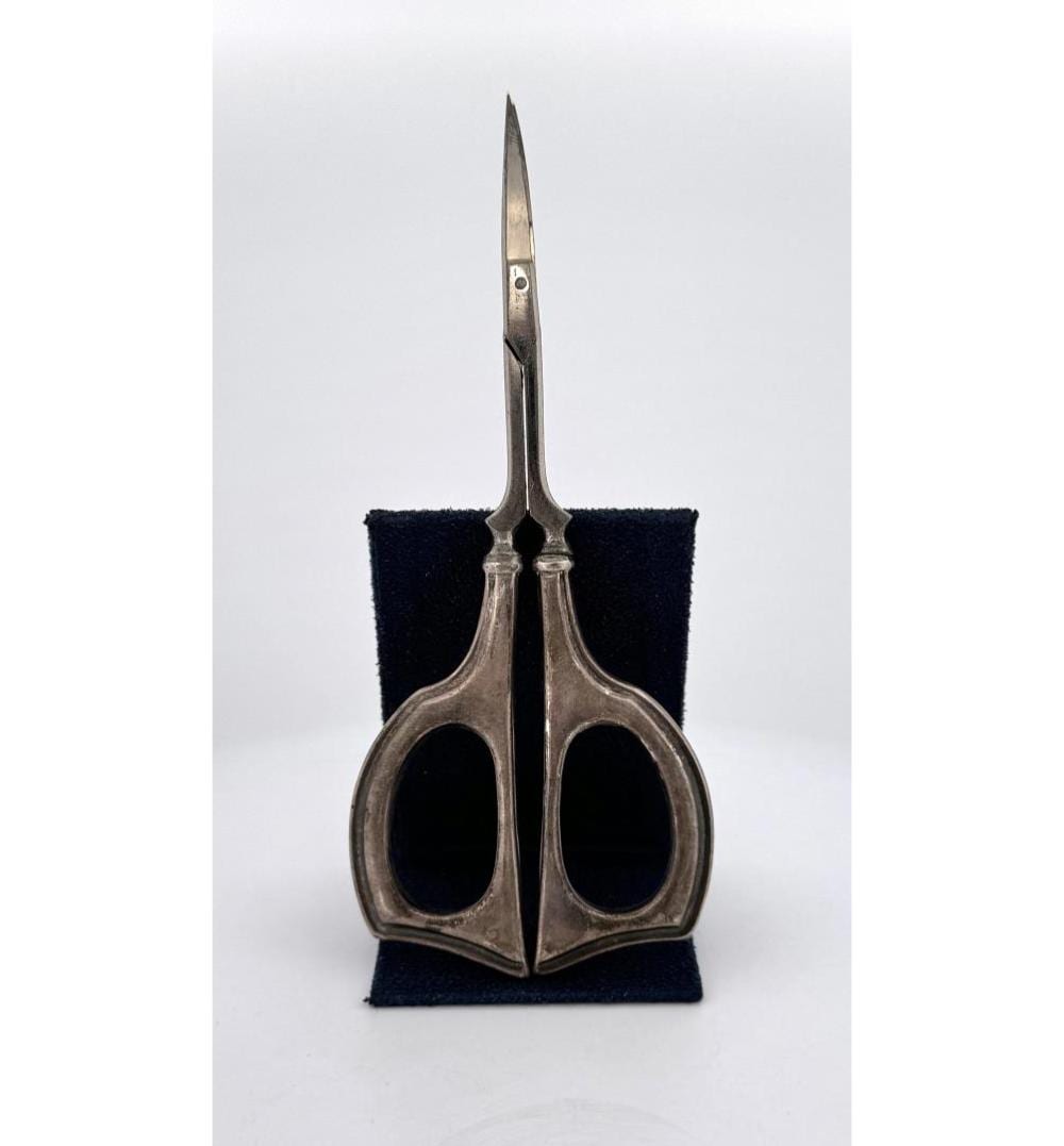 Close-up of metal embroidery scissors with finger loops and narrow blades, resting on a dark fabric stand.