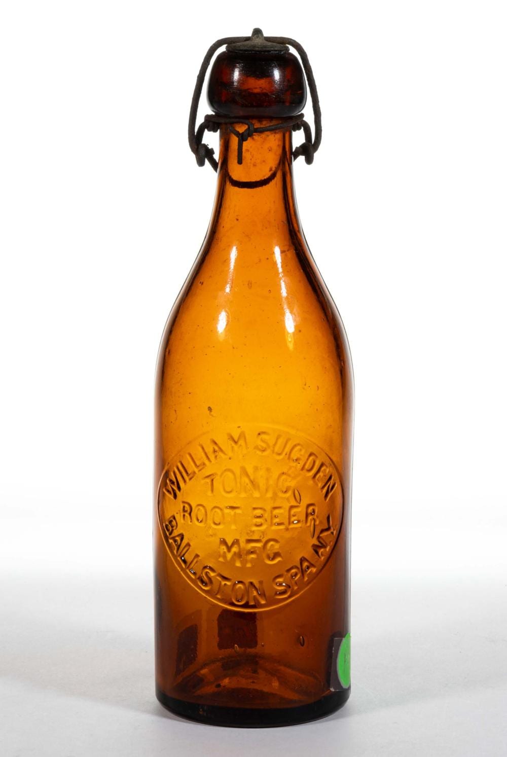 Amber glass soda bottle with a dark metal wire bail and embossed label reading “TONIC ROOT BEER.”
