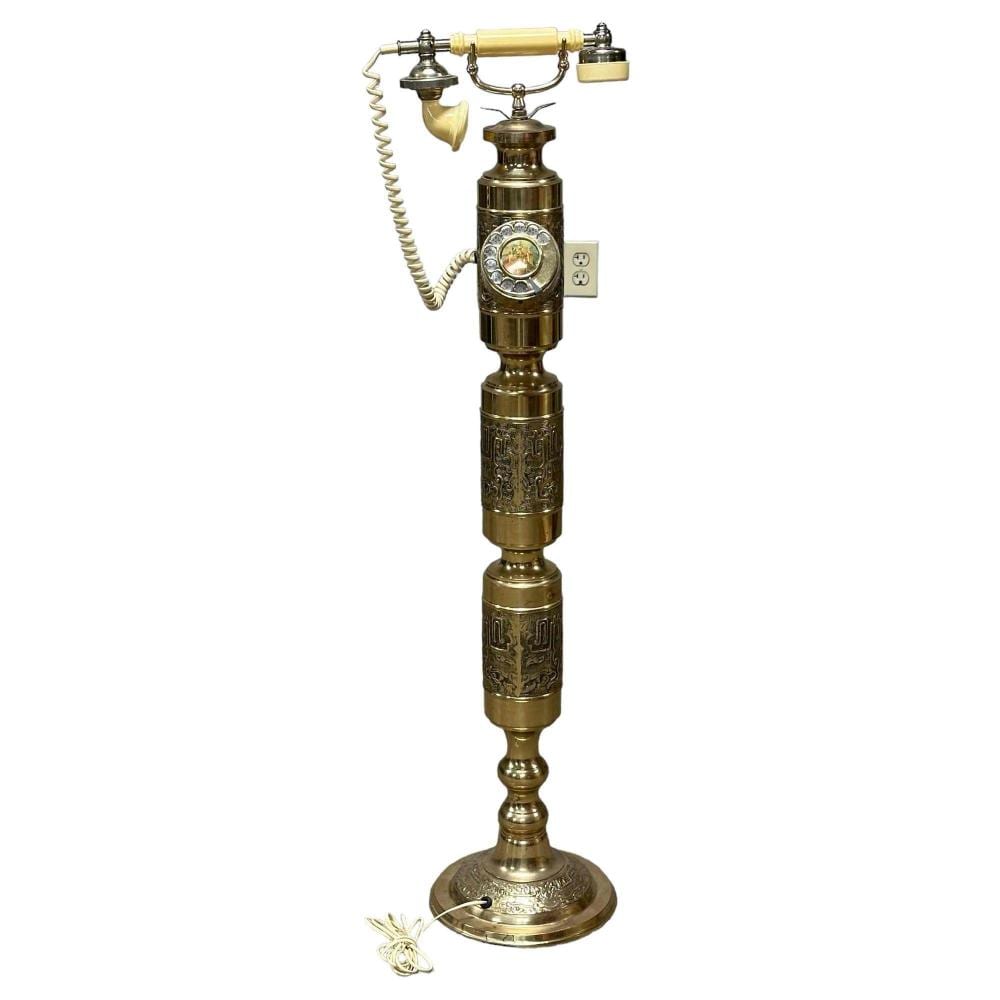 Antique-style brass rotary telephone on a pedestal with a handset and coiled cord, shown against a white background.