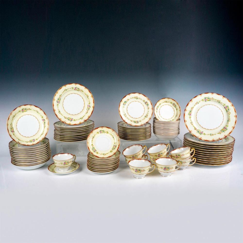 Assorted white china tableware set with gold rims and small pink floral accents, including plates, bowls, and teacups on a display table.