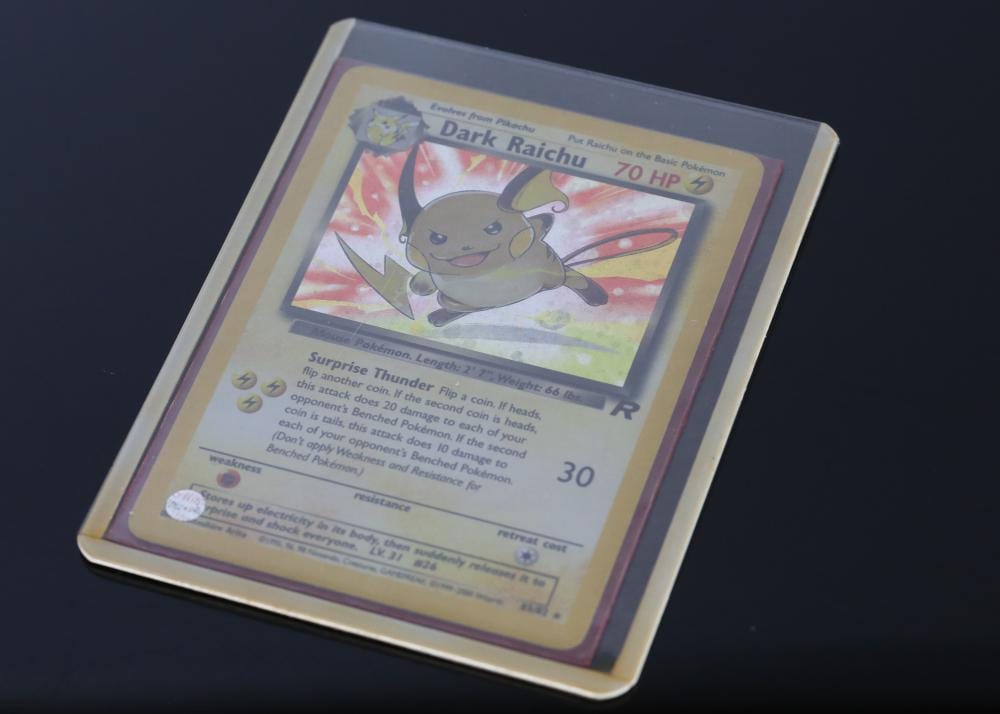 Trading card showing a Pokémon character labeled “Dark Raichu” with “70 HP” and colorful card artwork, photographed at an angle on a dark background.