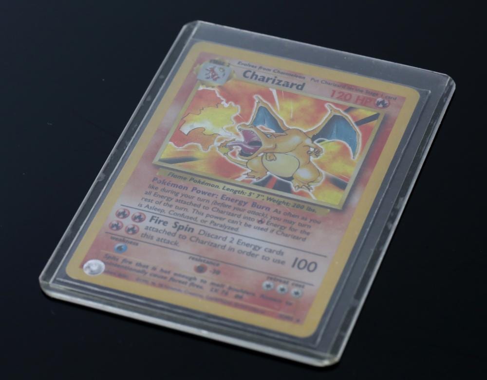 Pokemon trading card featuring Charizard with a holographic effect, displayed in a clear plastic sleeve on a dark background.
