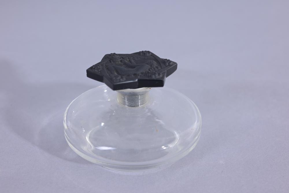 Clear glass perfume bottle with a dark decorative cap, shown against a light background.