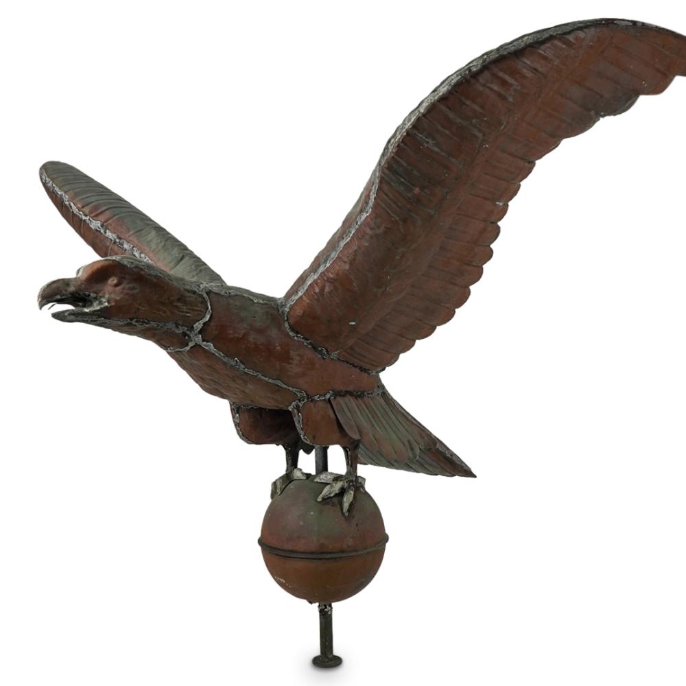 Metal eagle weathervane with outstretched wings and a round base on a pointed post.