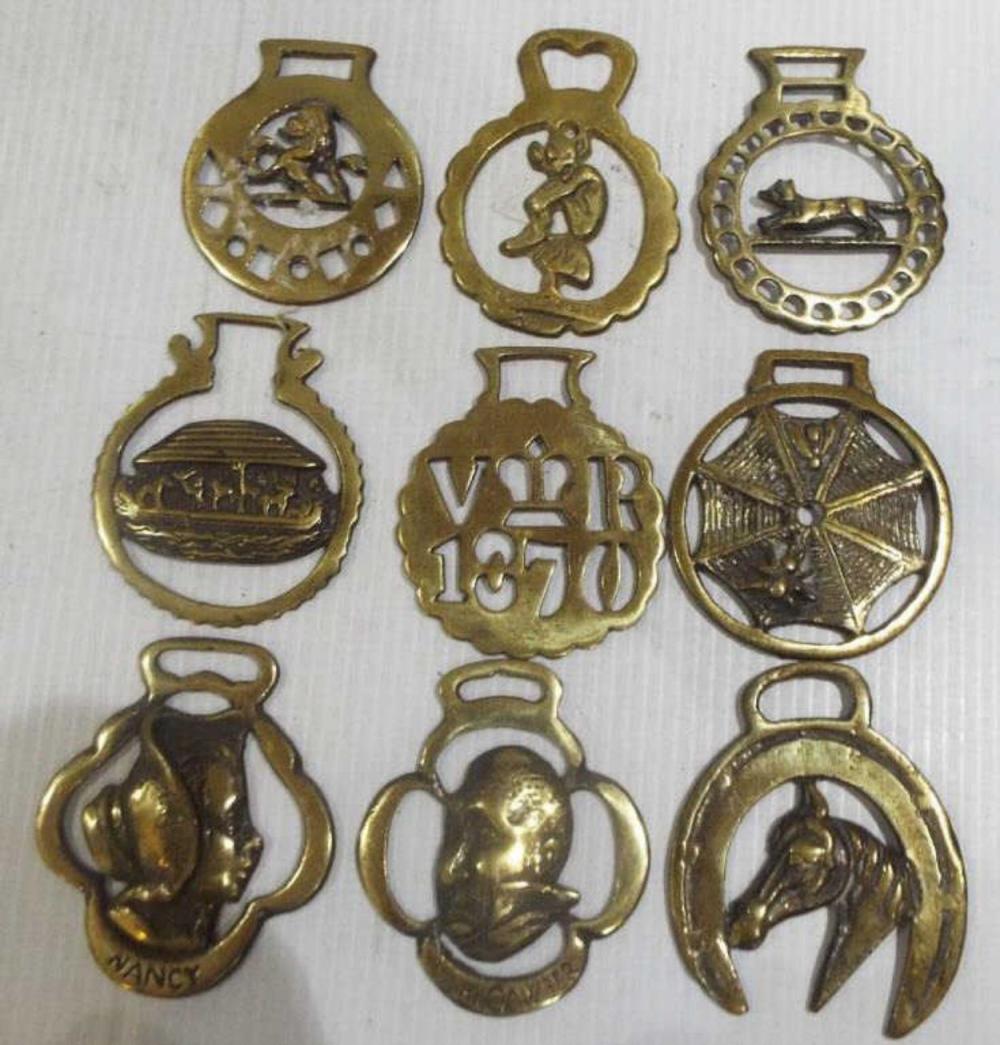 Nine gold-colored horse harness brass medallions and decorative plaques with horseshoe, wheel, and horse figure designs.