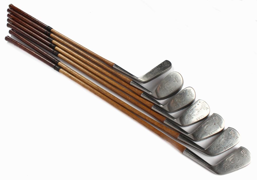 Set of five antique-style golf club irons with wooden shafts and silver club heads, shown together on a white background.