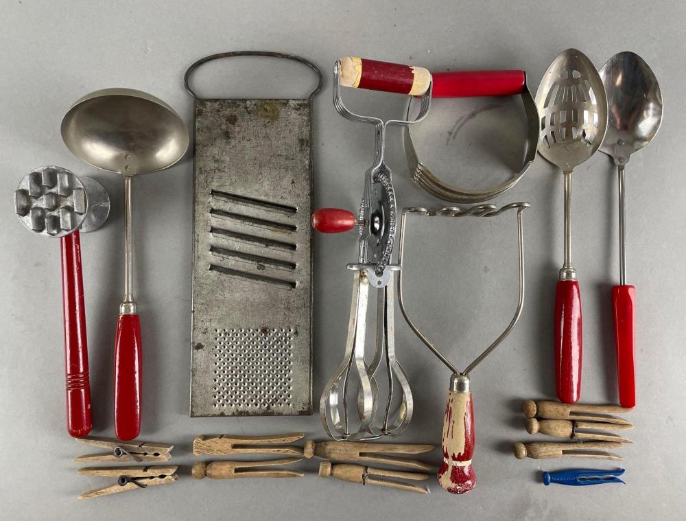 Assorted vintage kitchen utensils on a gray background, including a grater, hand tools with red handles, a potato masher, spoons, and ladles.