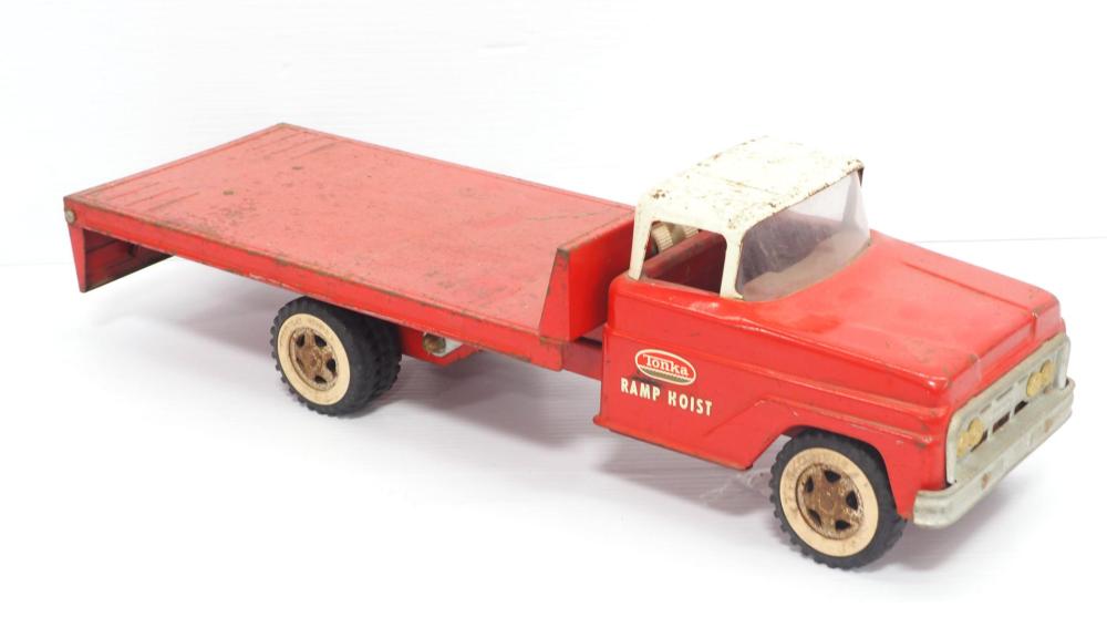 Red toy pickup truck with a flat trailer bed ramp hoist and black wheels, shown in side view on a white background.