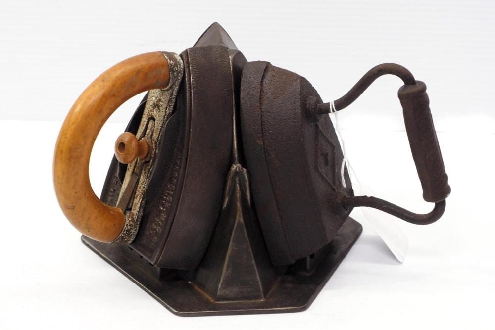 Cast iron sad iron trivet with a wooden handle and three hinged sections, photographed on a white background.
