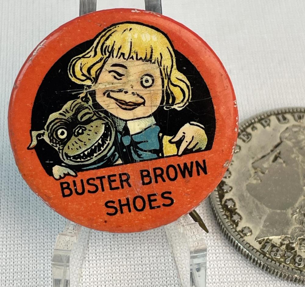 Round red advertising pinback button with a cartoon girl holding a shoe and the text “BUSTER BROWN SHOES.”