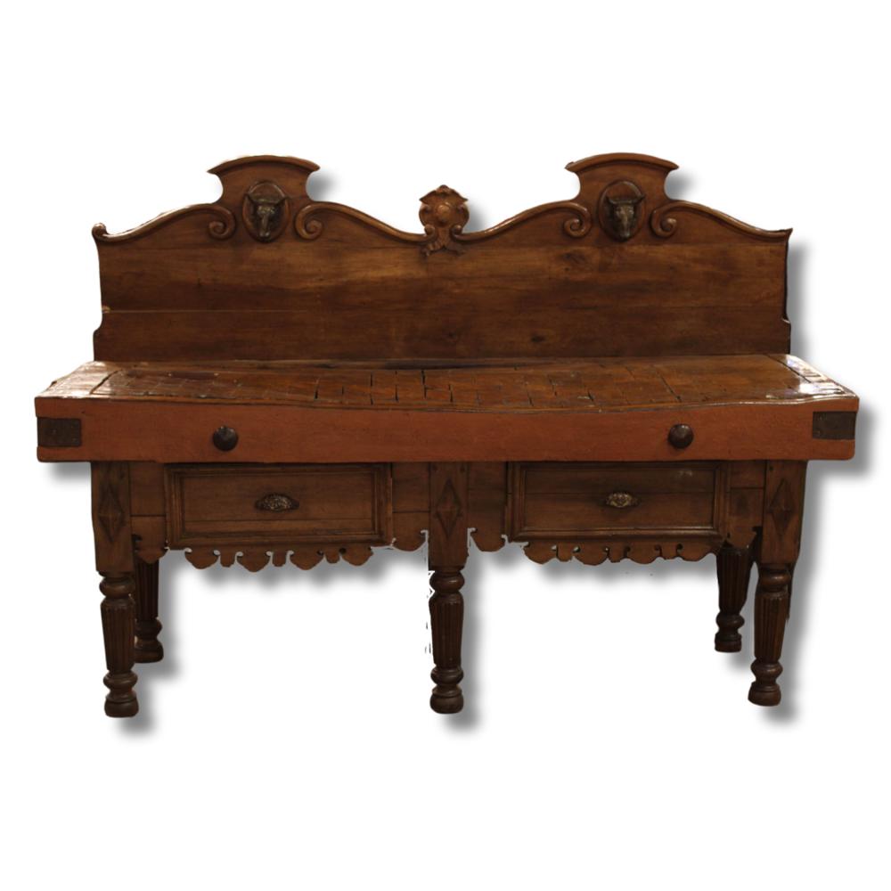 Antique-style wooden butcher block table with carved apron and drawers, shown front view against a white background.