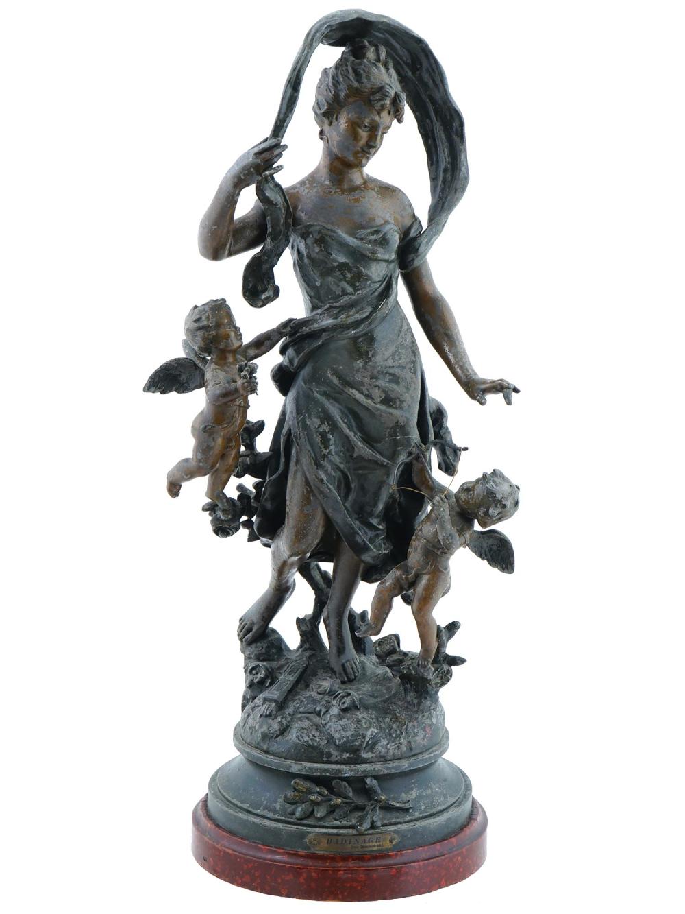 Bronze-colored sculpture of a woman holding a child-like figure and standing among multiple small figures, on a circular base.