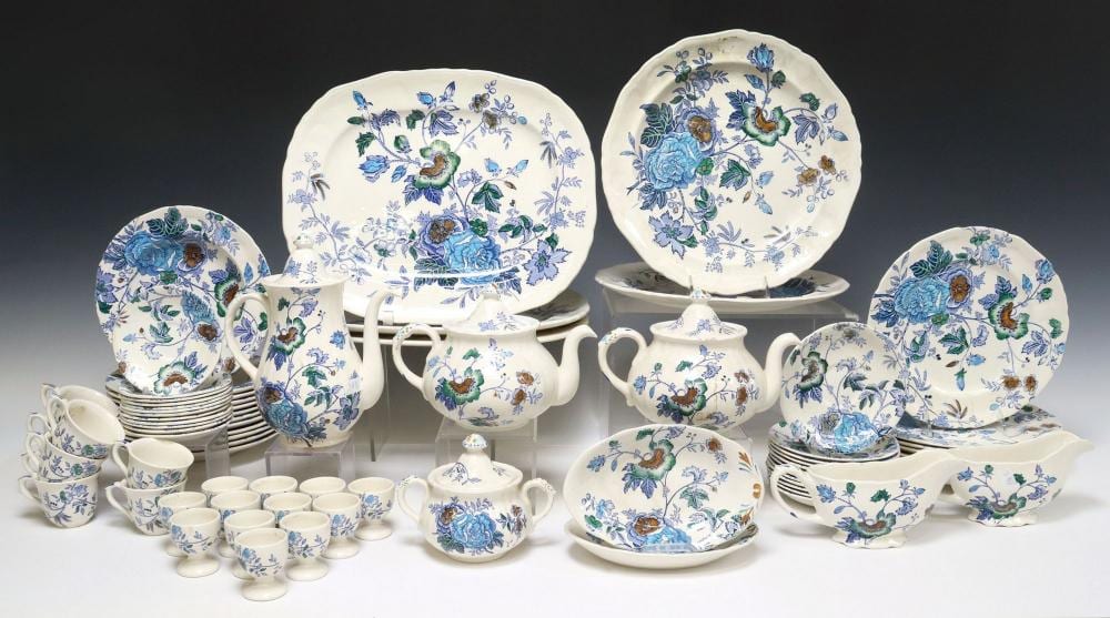 Group of blue-and-green floral dinnerware pieces with molded serving dishes, teapots, cups, and plates arranged on a white display.