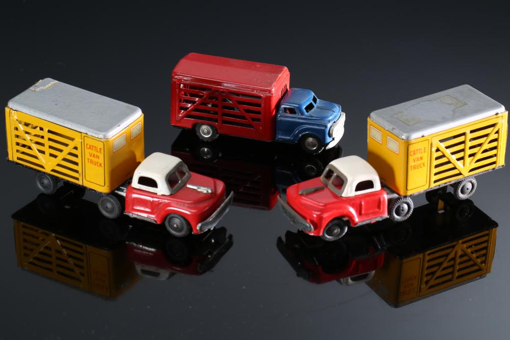 Three vintage tin toy trucks in yellow and red with a blue truck, shown on a black reflective surface.