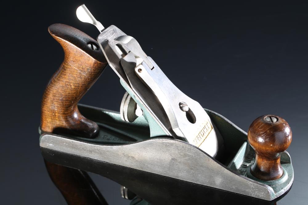 Hand plane tool with a wooden handle and a metal body, shown at an angle against a dark background.