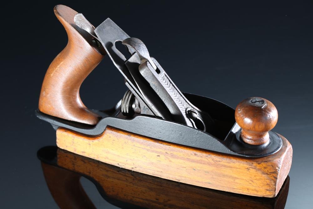 Wood-bodied hand plane with an iron cutting blade, wooden handle, and metal components shown against a dark background.