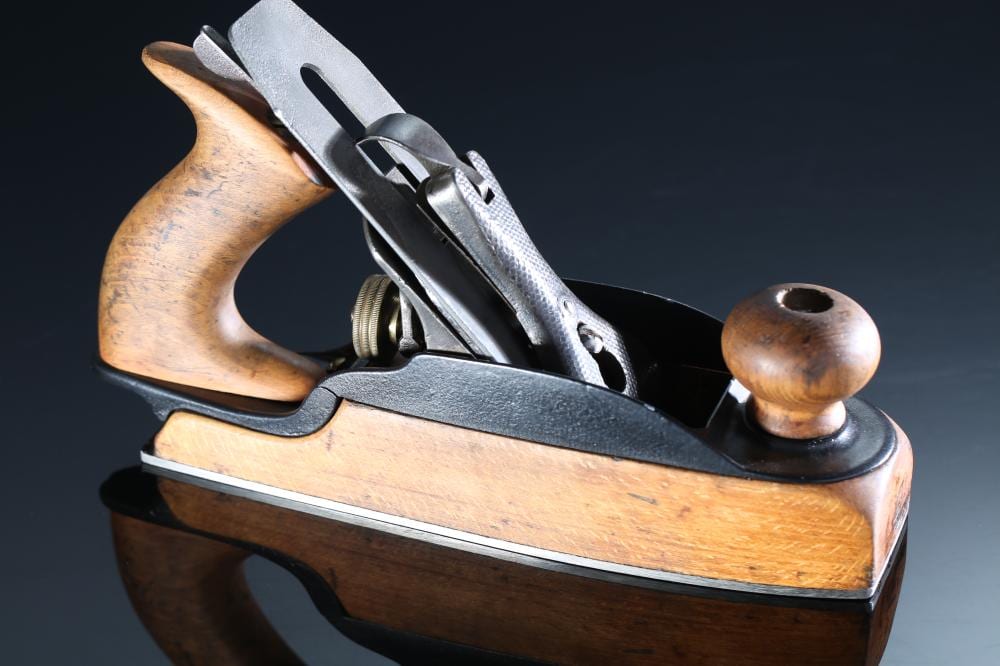 Antique-style woodworking hand plane with a wooden body, metal blade assembly, and a curved wooden handle on a dark background.