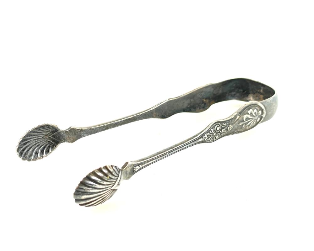 Vintage silver-colored ice tongs with seashell-shaped ends and engraved decorative scrollwork.