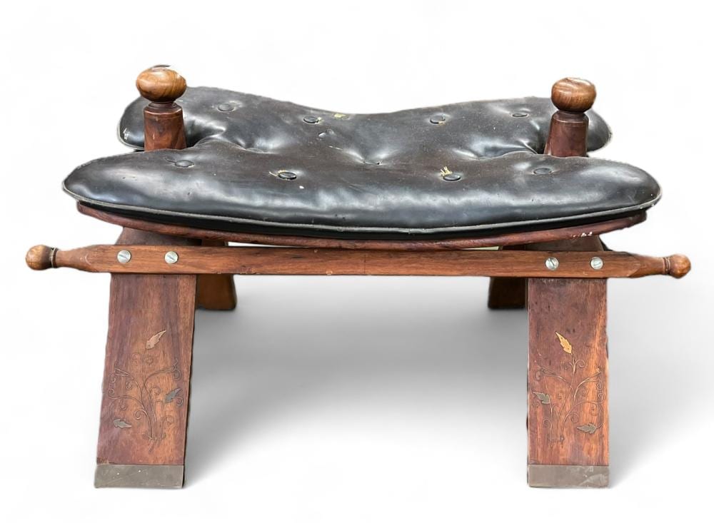 Vintage wooden saddle-shaped stool with dark gray leather-like seat, metal studs, and two turned wooden post supports with finials.
