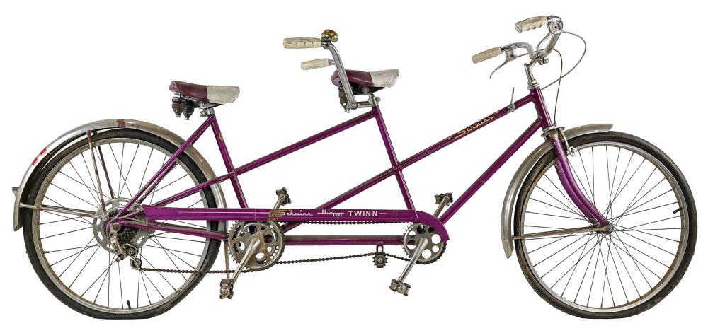 Purple vintage tandem bicycle with two seats and handlebars, showing front and rear wheels and drivetrain components on a white background.