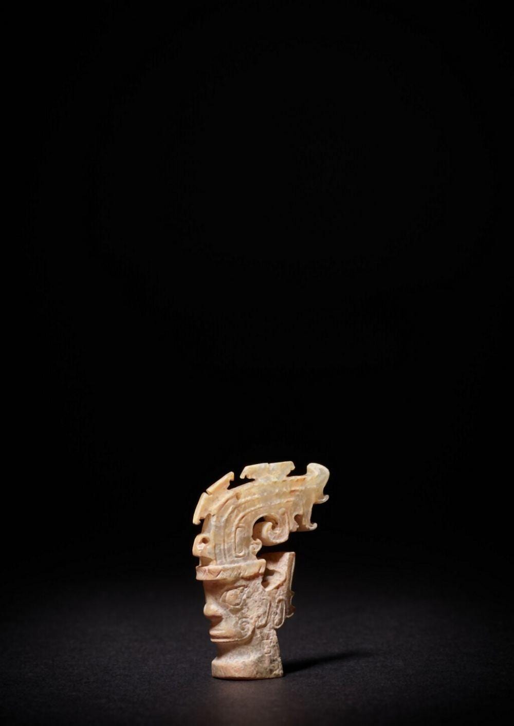 An exceptionally rare jade 'mask' ornament, Shang dynasty or earlier | 商或較早 卷尾形高冠神人首玉飾 comparable sale