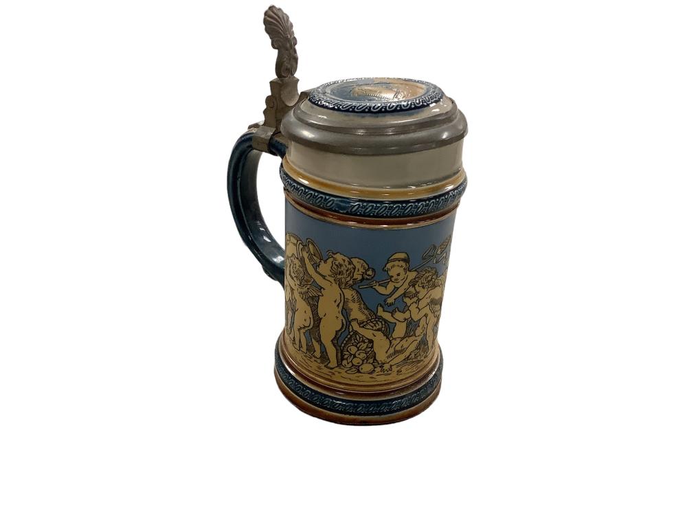 Ceramic beer stein with a blue and tan painted scene, dark handle, and a metal lid with a finial knob.