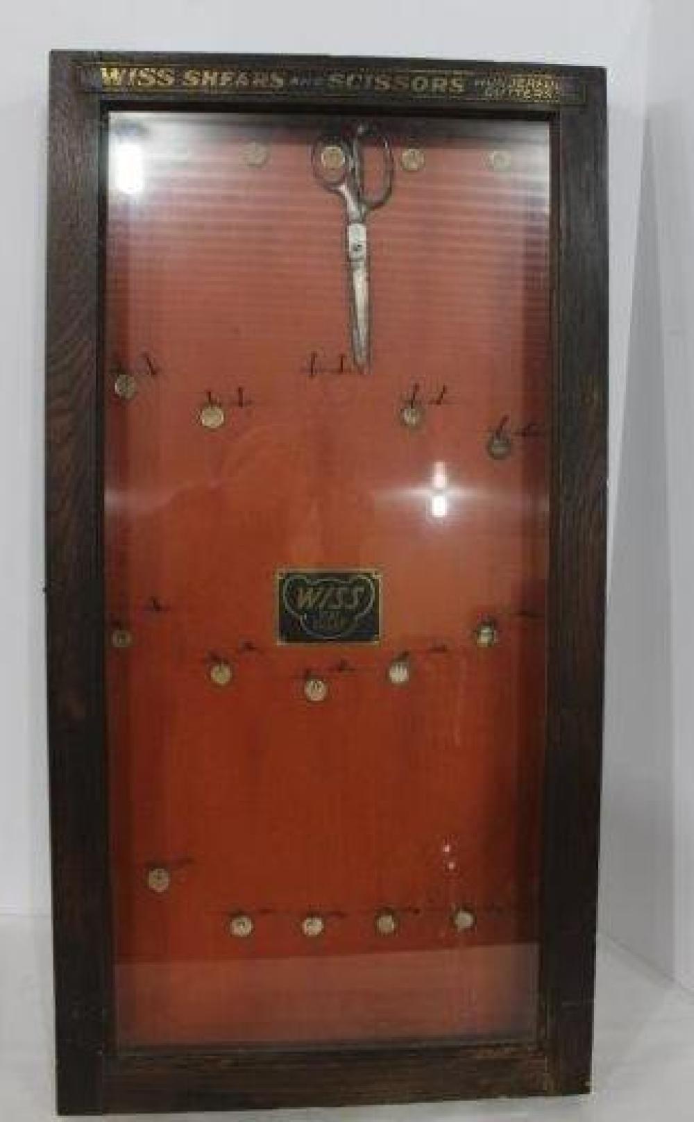 Wooden hanging display case with scissors and shears branding across the top, showing hanging metal scissors on a red backing.
