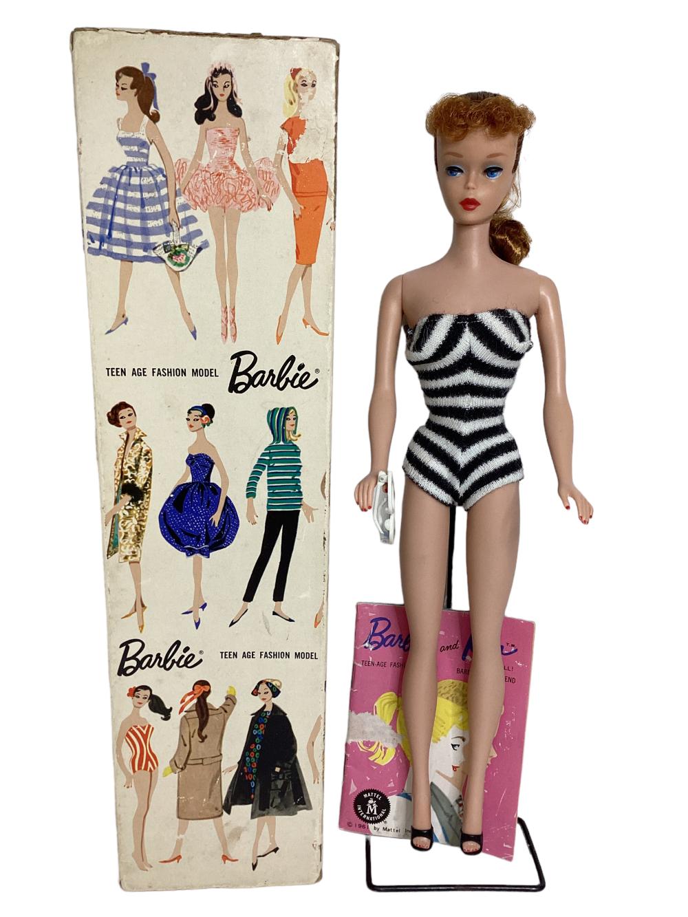 Barbie fashion model doll with red-brown hair wearing a black-and-white striped strapless romper, standing next to a retail box.