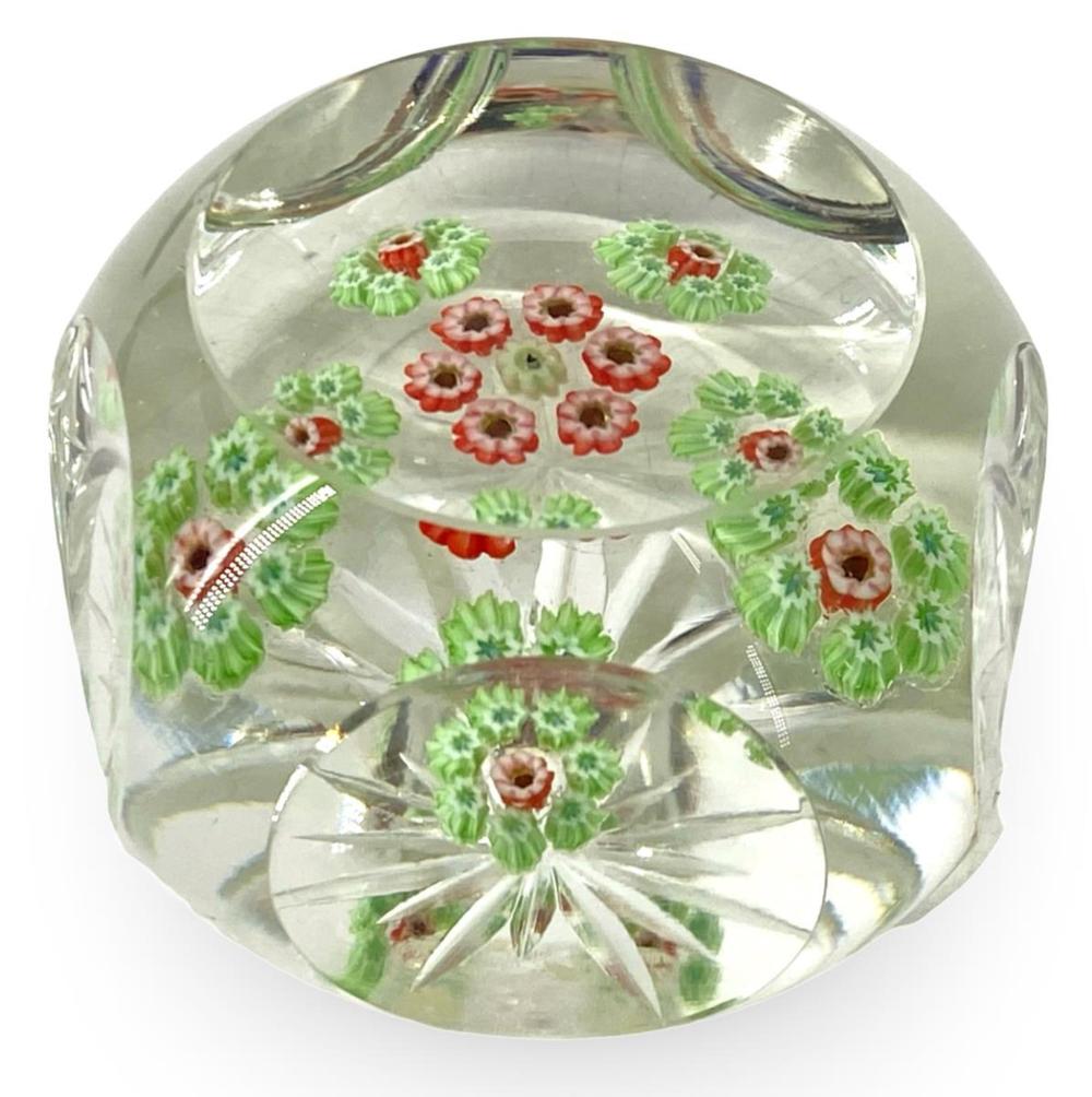 Clear glass paperweight with embedded red and green flower and leaf designs, faceted base, and beveled edges.