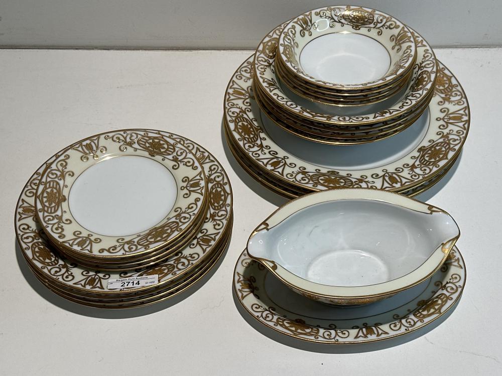Set of white porcelain plates and bowls with gold and dark green ornamental scroll and floral designs, stacked on matching serving platters.