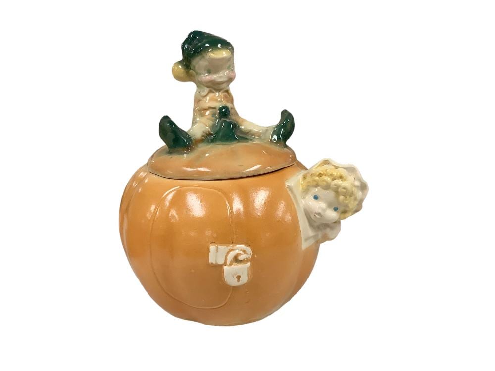 Small ceramic cookie jar shaped like a boy in a green hat standing behind a pumpkin-shaped lid with an orange face and handle.