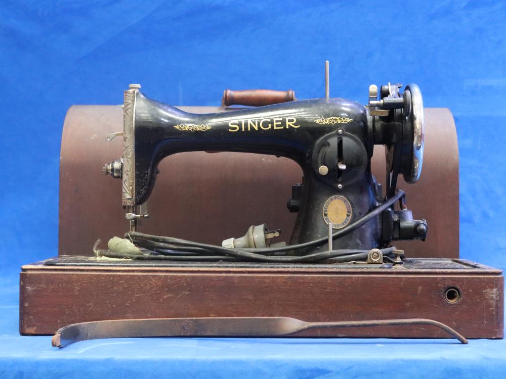 Black Singer sewing machine with gold lettering and metal parts mounted in an open wooden case on a blue background.